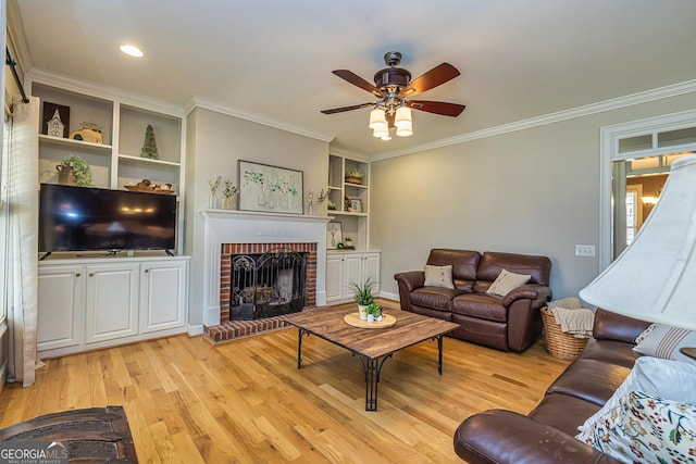 living room with a ceiling fan, light wood-style flooring, ornamental molding, a brick fireplace, and built in shelves