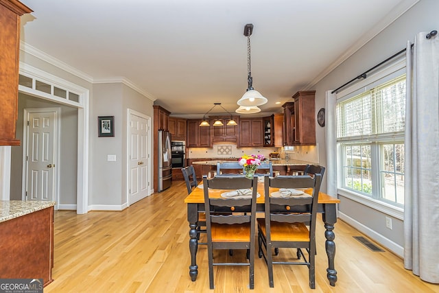 dining room featuring light wood-type flooring, visible vents, crown molding, and baseboards