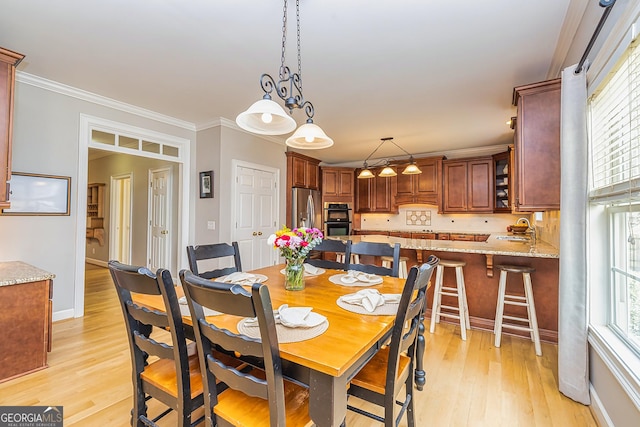 dining area featuring light wood-type flooring, a healthy amount of sunlight, and ornamental molding