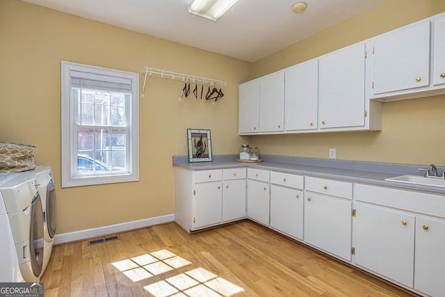 kitchen with visible vents, light wood-style flooring, white cabinets, a sink, and separate washer and dryer