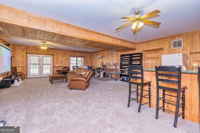 living room with carpet floors, wood walls, visible vents, and a ceiling fan