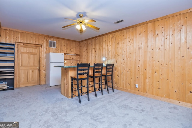 kitchen with carpet floors, freestanding refrigerator, visible vents, and wooden walls