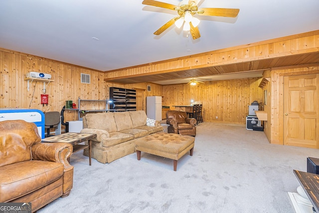 carpeted living room with ceiling fan, wooden walls, and visible vents