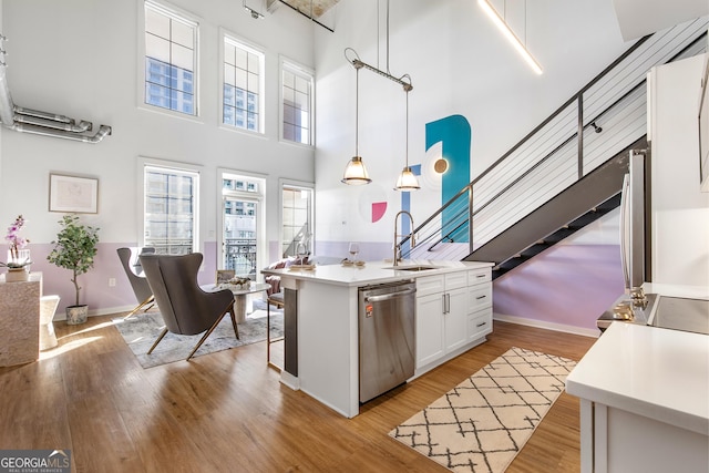 kitchen featuring light wood-style flooring, light countertops, stainless steel dishwasher, white cabinetry, and a sink