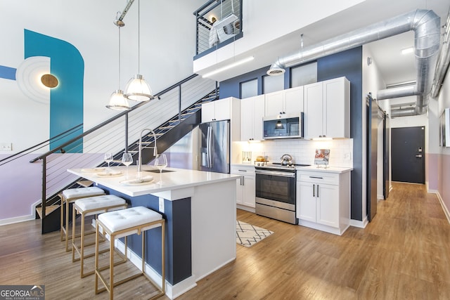 kitchen featuring light countertops, a towering ceiling, appliances with stainless steel finishes, light wood-style floors, and a kitchen bar