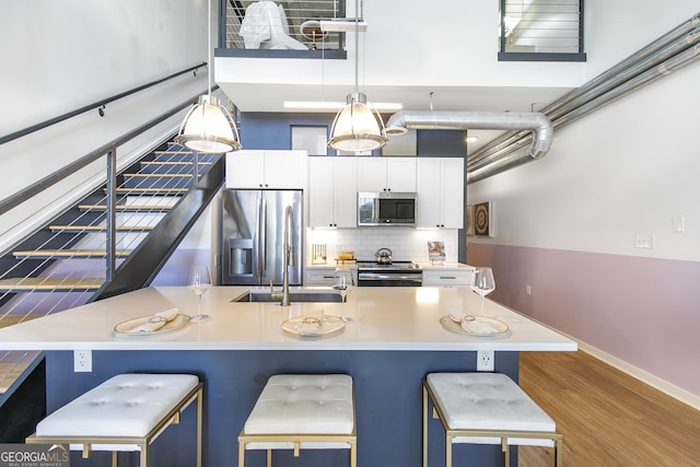 kitchen with a breakfast bar area, wood finished floors, white cabinetry, appliances with stainless steel finishes, and decorative backsplash