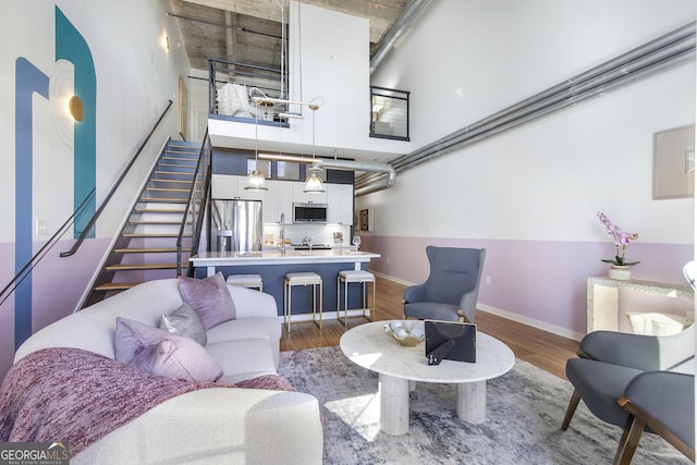 living area with wood finished floors, a towering ceiling, baseboards, and stairs