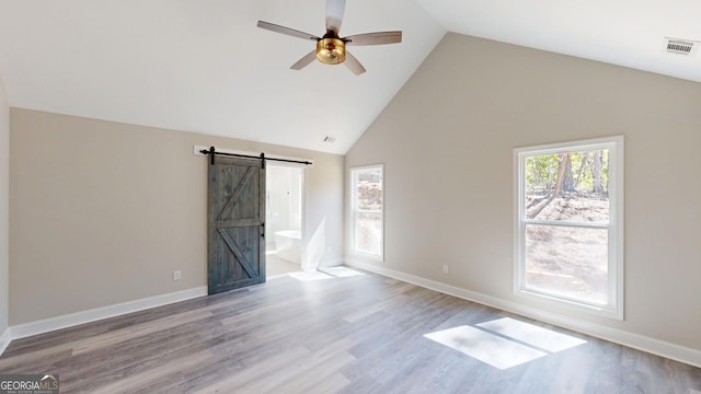 unfurnished room featuring ceiling fan, a barn door, wood finished floors, visible vents, and baseboards