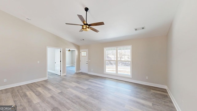 empty room featuring light wood-style flooring, visible vents, vaulted ceiling, and baseboards