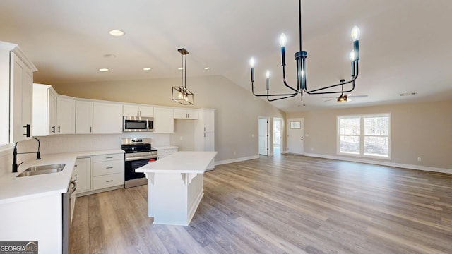 kitchen featuring appliances with stainless steel finishes, a center island, light countertops, white cabinetry, and a sink