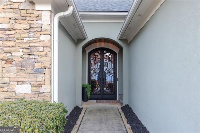 entrance to property featuring stone siding, a shingled roof, french doors, and stucco siding