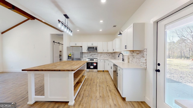 kitchen with a barn door, a kitchen island, appliances with stainless steel finishes, wooden counters, and a sink