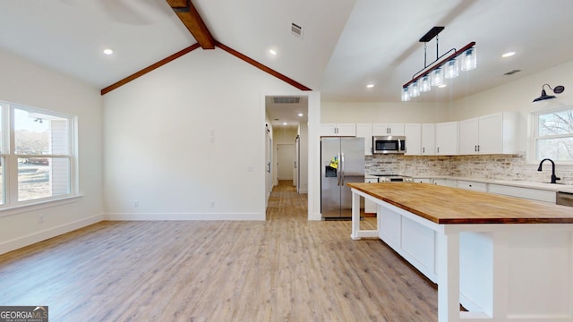 kitchen with vaulted ceiling with beams, visible vents, backsplash, appliances with stainless steel finishes, and butcher block countertops