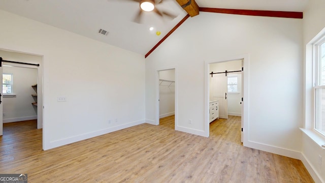 unfurnished bedroom featuring a walk in closet, visible vents, light wood-style flooring, a barn door, and beamed ceiling