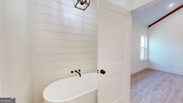 bathroom featuring vaulted ceiling, wood finished floors, a freestanding tub, and baseboards