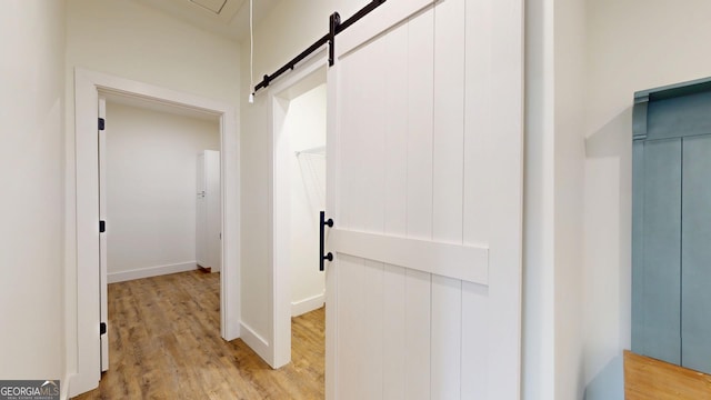 hall with elevator, a barn door, baseboards, and light wood finished floors