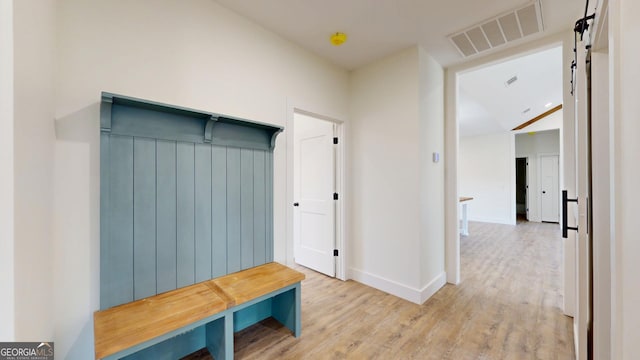 mudroom with baseboards, a barn door, visible vents, and wood finished floors