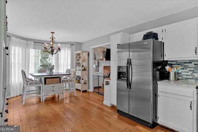 kitchen with light wood-style floors, white cabinetry, stainless steel refrigerator with ice dispenser, and tasteful backsplash