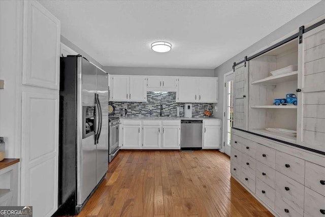 kitchen featuring a barn door, stainless steel appliances, light countertops, white cabinetry, and a sink