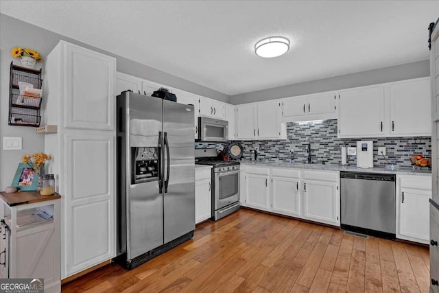 kitchen with stainless steel appliances, tasteful backsplash, light wood-style floors, white cabinetry, and a sink