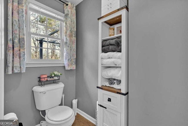 bathroom featuring toilet, a wealth of natural light, and baseboards