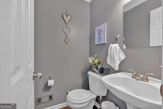 half bath featuring toilet, a sink, visible vents, and baseboards