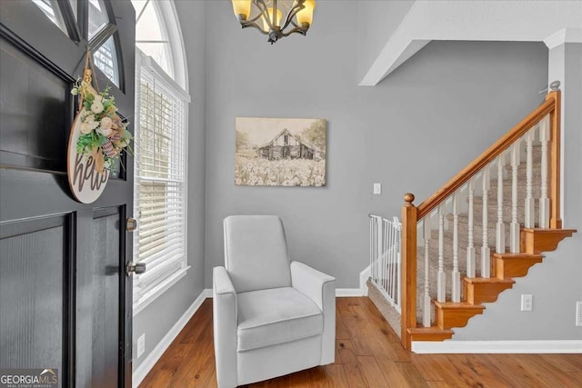 living area featuring stairway, an inviting chandelier, wood finished floors, and baseboards