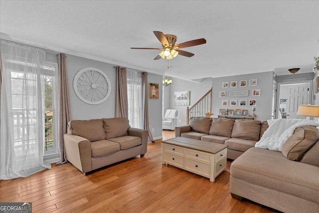 living room with ornamental molding, stairway, light wood finished floors, and ceiling fan with notable chandelier