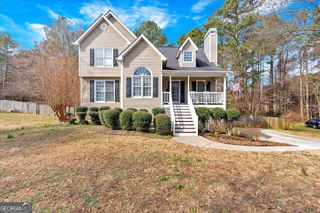 traditional-style house with covered porch, a chimney, fence, and a front lawn