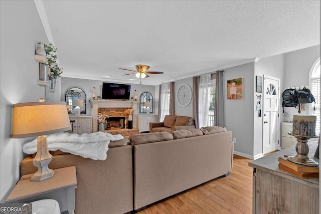 living area with light wood-type flooring, ceiling fan, ornamental molding, and a stone fireplace