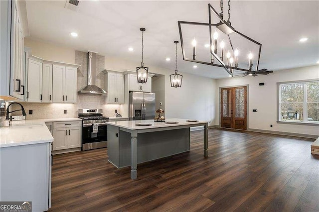 kitchen with wall chimney exhaust hood, a kitchen island, dark wood-type flooring, stainless steel appliances, and a sink