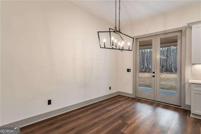 unfurnished dining area with lofted ceiling, a notable chandelier, dark wood-type flooring, baseboards, and french doors