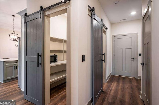 hall featuring dark wood-style floors, visible vents, baseboards, and a barn door