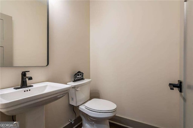 half bathroom with a sink, toilet, and baseboards