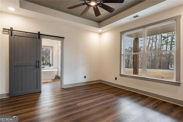 empty room featuring dark wood-style floors, a barn door, a raised ceiling, and visible vents