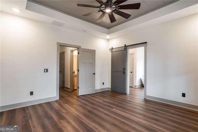 unfurnished bedroom with a barn door, baseboards, a raised ceiling, and dark wood-type flooring