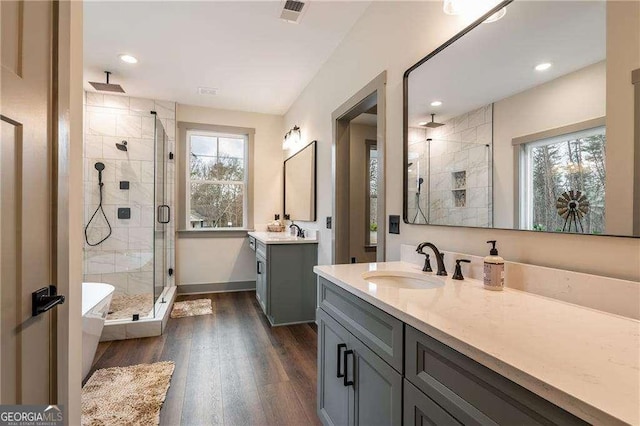 full bath featuring two vanities, visible vents, a sink, a shower stall, and wood finished floors