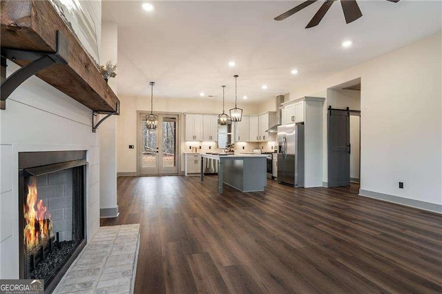 kitchen with a barn door, ceiling fan with notable chandelier, stainless steel fridge with ice dispenser, light countertops, and a center island