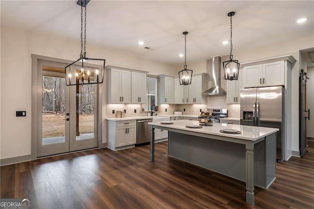 kitchen featuring wall chimney exhaust hood, appliances with stainless steel finishes, light countertops, and dark wood-style flooring