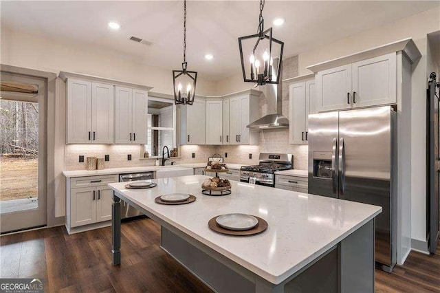 kitchen featuring visible vents, appliances with stainless steel finishes, a center island, wall chimney range hood, and a sink