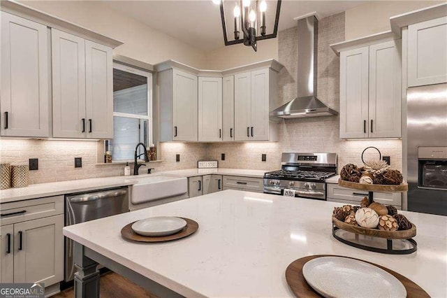 kitchen with decorative light fixtures, tasteful backsplash, appliances with stainless steel finishes, a sink, and wall chimney exhaust hood