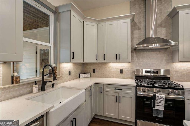 kitchen featuring stainless steel range with gas cooktop, light countertops, decorative backsplash, a sink, and wall chimney exhaust hood