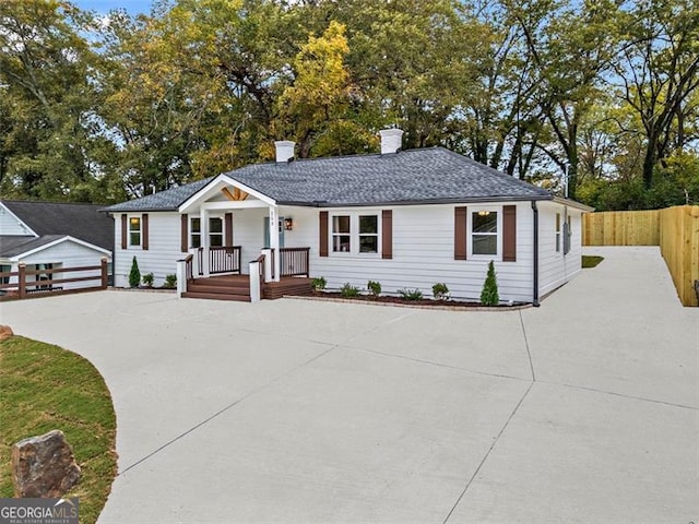 ranch-style house with roof with shingles, a chimney, a porch, fence, and an outdoor structure