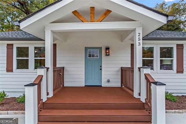 view of exterior entry featuring covered porch and a shingled roof