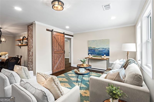 living room featuring visible vents, a barn door, ornamental molding, wood finished floors, and baseboards