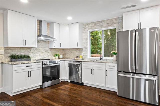 kitchen featuring light stone counters, visible vents, appliances with stainless steel finishes, a sink, and wall chimney range hood