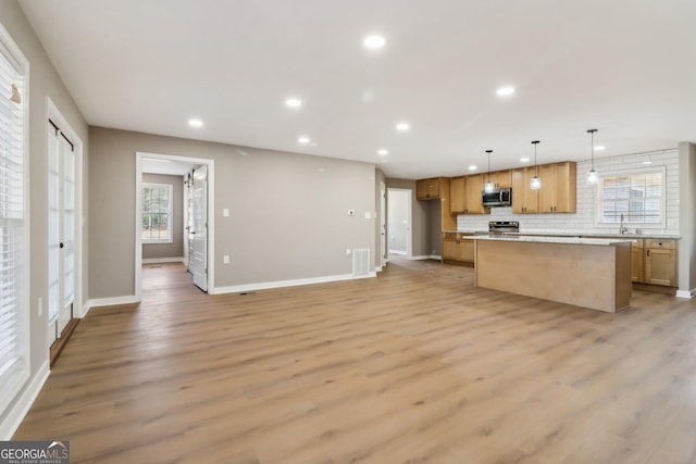 kitchen with a kitchen island, decorative backsplash, recessed lighting, light wood-style flooring, and appliances with stainless steel finishes