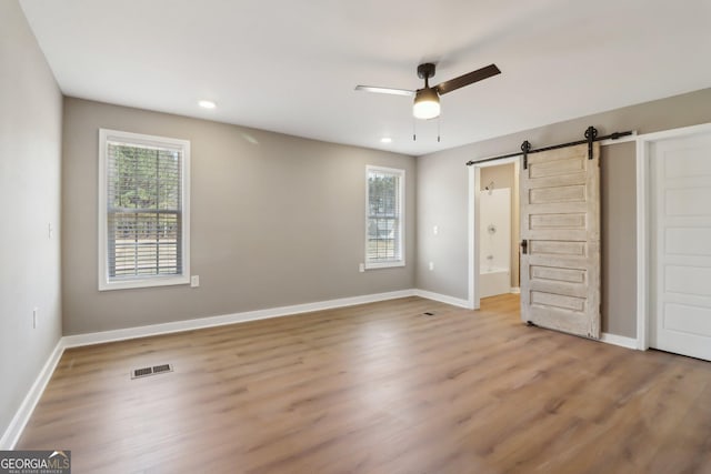 unfurnished bedroom featuring visible vents, multiple windows, baseboards, and a barn door