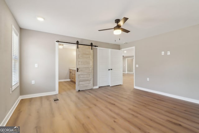 unfurnished bedroom featuring a barn door, baseboards, visible vents, and light wood finished floors