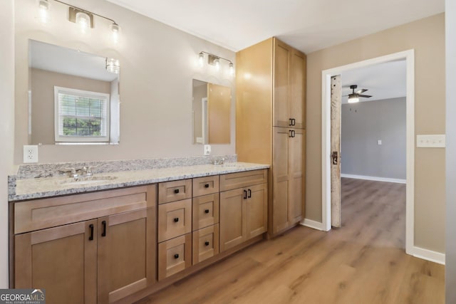 bathroom with a ceiling fan, a sink, wood finished floors, double vanity, and baseboards